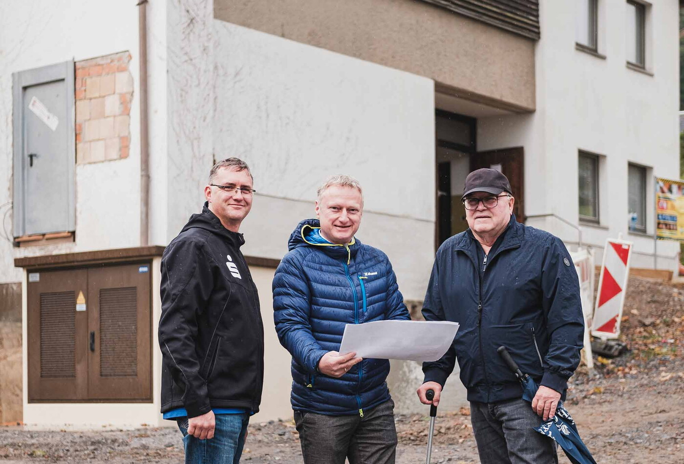 Drei Männer stehen vor einen Gebäude und schauen in die Kamera.