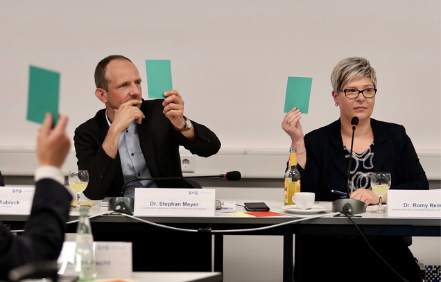 Mehrere Personen stimmen mittels grüner Karten ab.