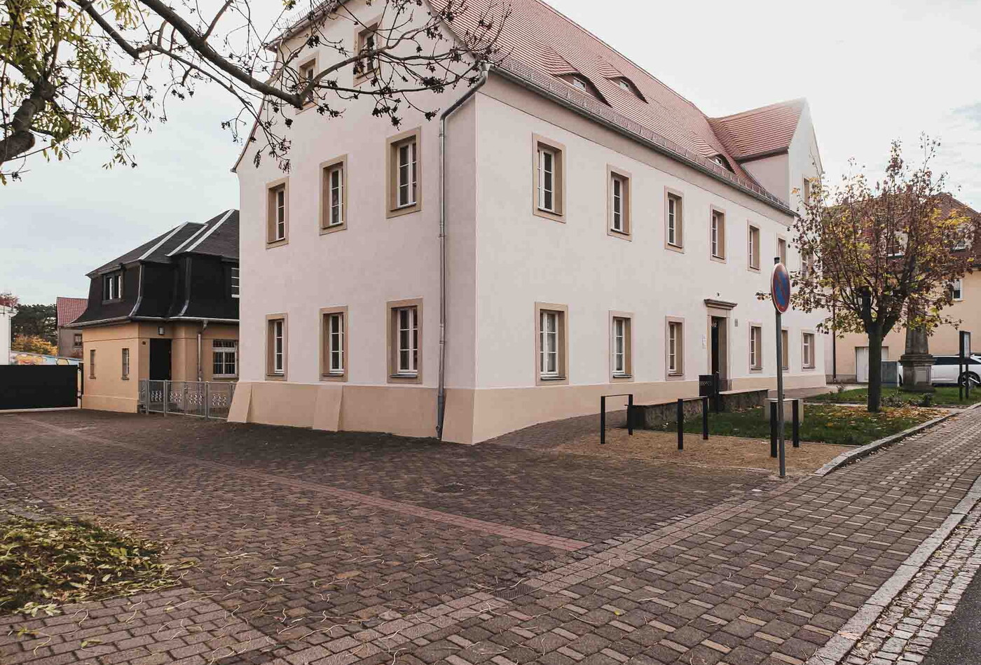 Ein weißes großes Gebäude und davor ist ein gepflasterter Weg.
