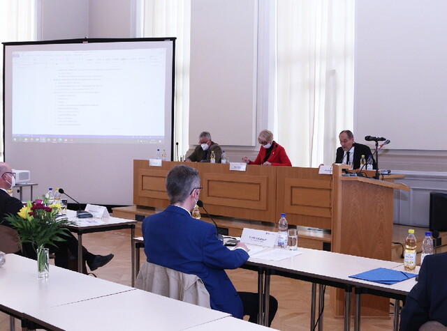Seitenansicht auf den Konferenzraum wo die Personen auf ihren Plätzen sitzen