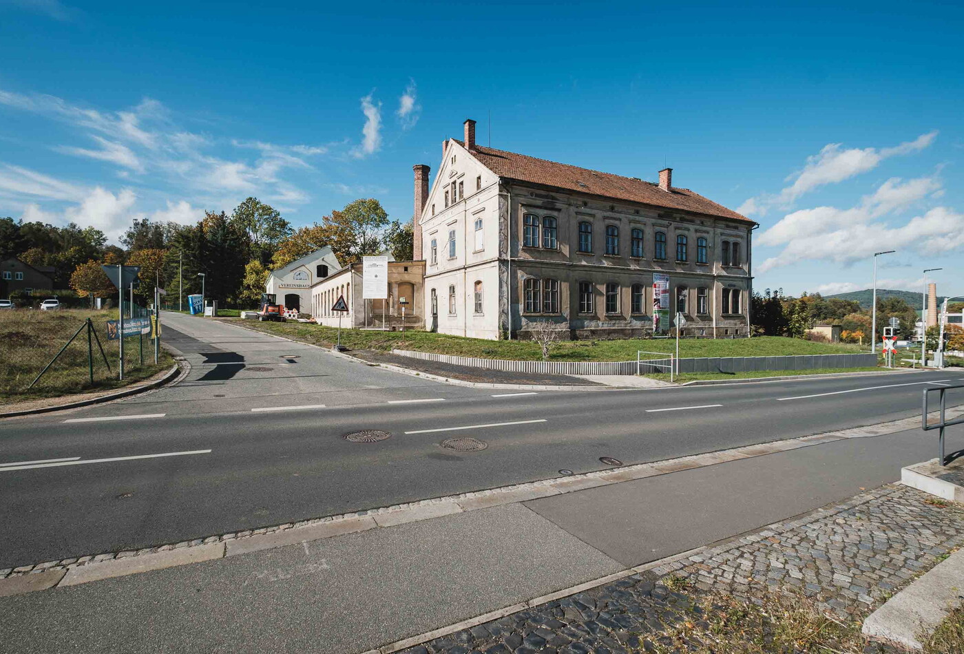 Auf dem Bild ist im Vordergrund eine Kreuzung und dahinter ein altes Haus