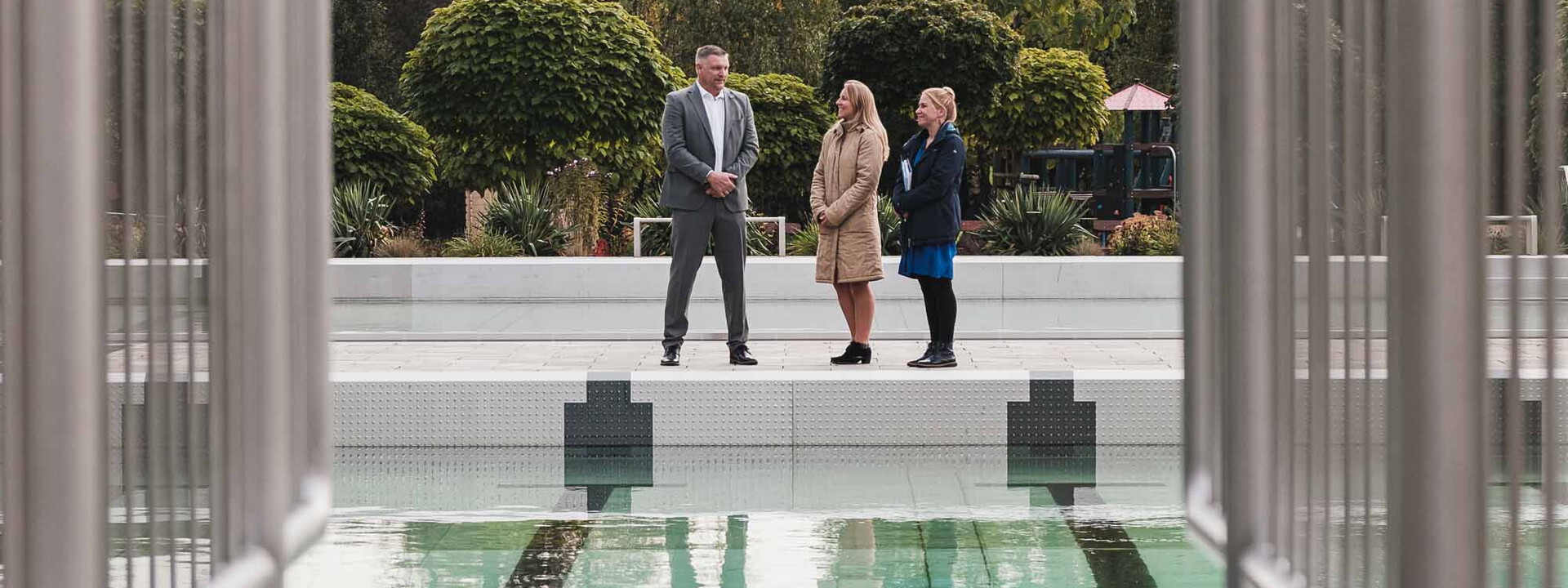 Im Vordergrund ist ein Pool abgebildet und im Hintergrund stehen drei Personen
