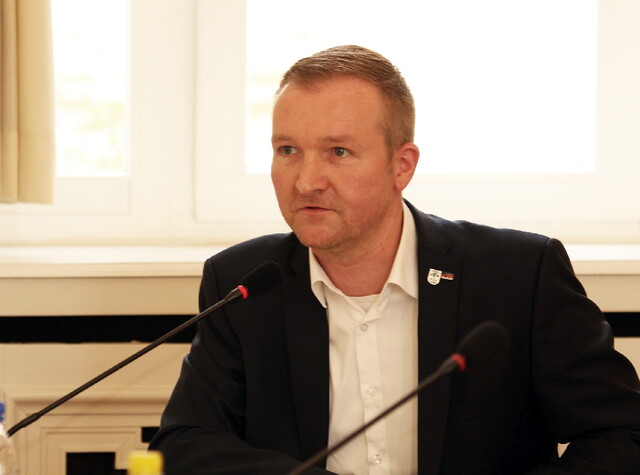 ein Mann sitzt am Pult und hält eine Rede