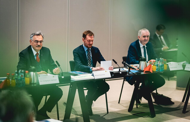 Michael Kretschmer und zwei weitere Männer bei einer Konferenz.