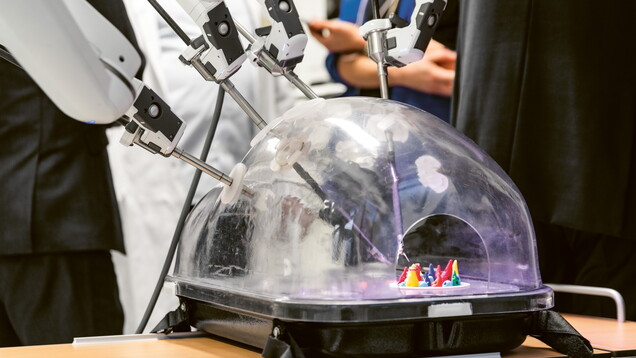 Personen stehen um einen  Roboter, dessen Greifarme arbeiten