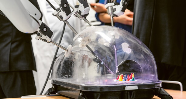 Personen stehen um einen  Roboter, dessen Greifarme arbeiten