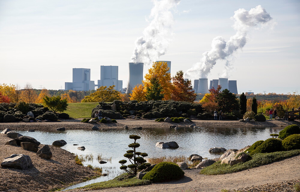 Ein herbstlicher Park mit einem Kraftwerk im Hintergrund.