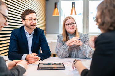 zwei Frauen und zwei Männer sitzen gemeinsam an einem Tisch mit Unterlagen.