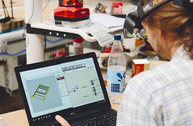 ein Mann sitzt vor einen Laptop auf dem ein 3D Modell abgebildet ist.