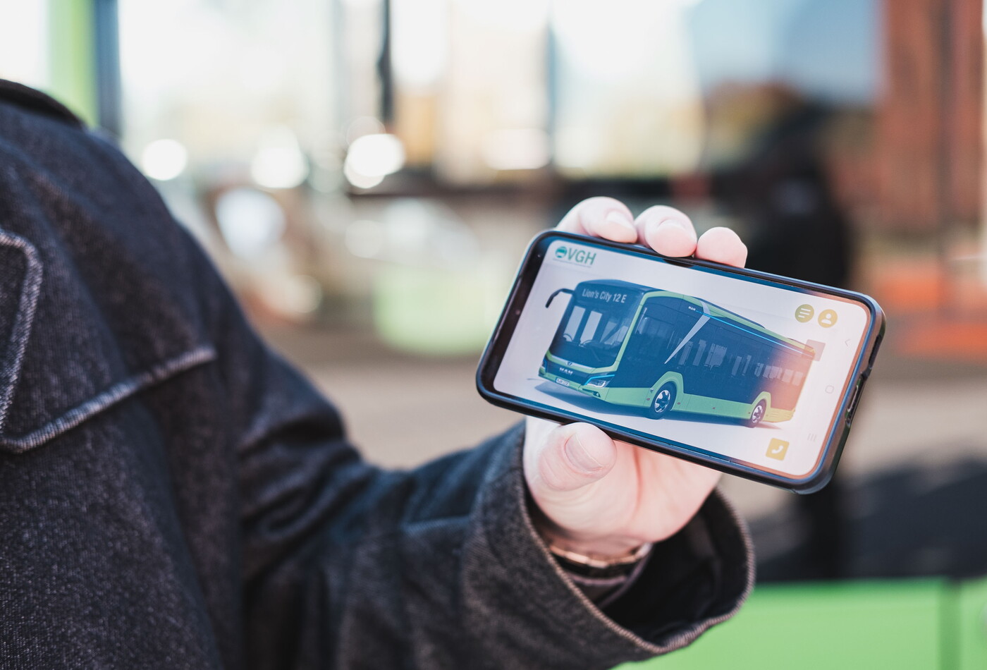 Eine Nahaufnahme wie eine Person ein Handy in den Händen hält und auf dem Handy ist ein grüner Bus abgebildet.