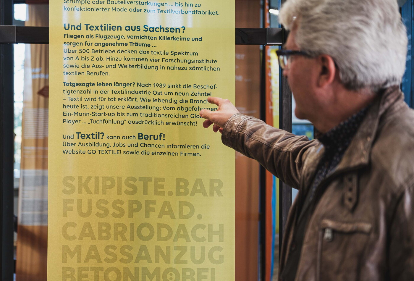 ein älterer Mann zeigt auf ein gelbes Poster