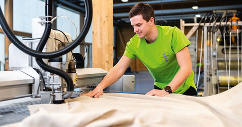 ein Mann im grünen T-Shirt näht den Stoff mit einer Maschine zurecht.