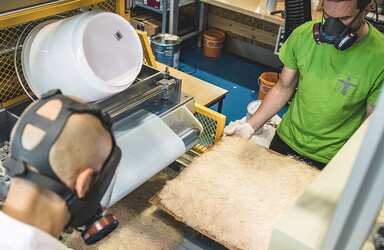ein  Mann im grünen T-Shirt steht an einer Maschine mit den vielen Fasern.