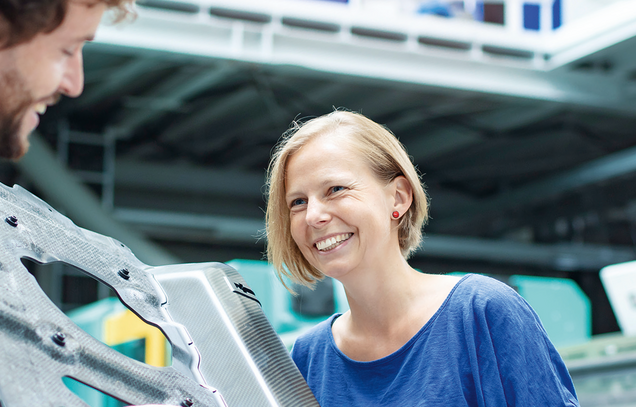 Eine Frau und ein Mann schauen sich ein Metallbauteil an.