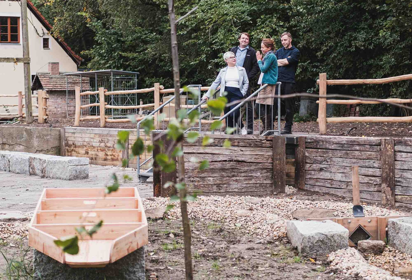 ein Garten und im Hintergrund stehen vier Personen die sich unterhalten.
