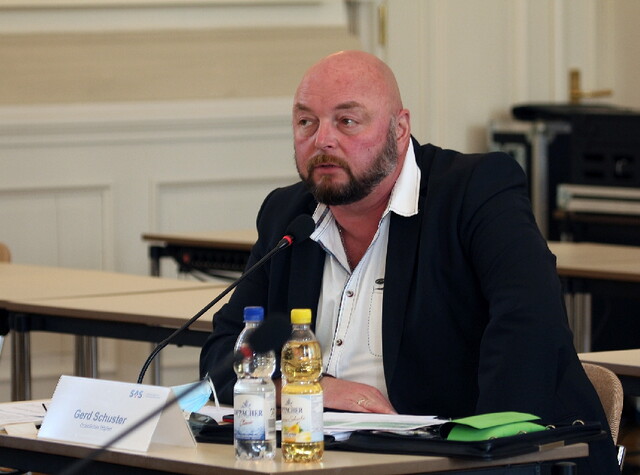 Herr Gerd Schuster sitzt an einem Tisch mit Mikrofon