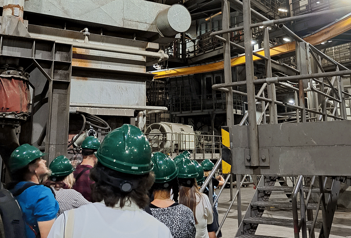 Schüler mit dunkelgrünen Kopfschutz laufen in eine Fabrik.