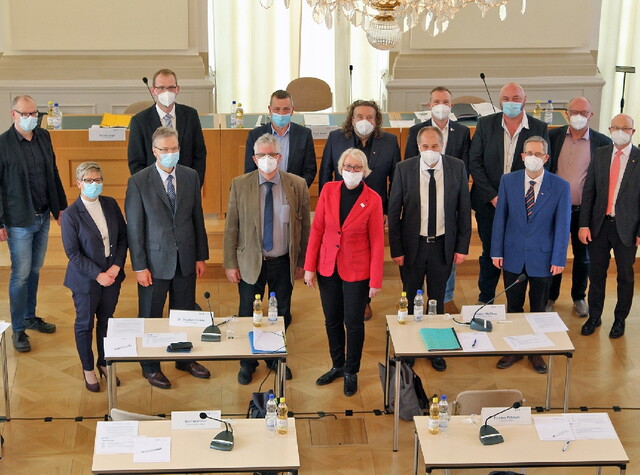 Personen mit OP-Masken schauen zu Kamera. Sie befinden sich einem Konferenzraum