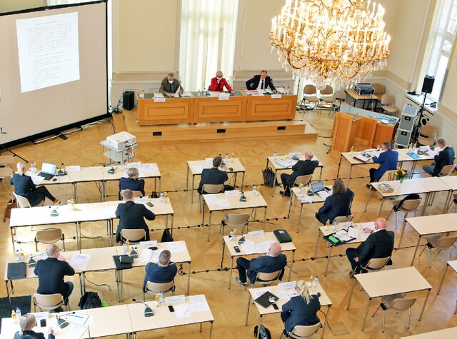 zusehen ist die Draufsicht auf den Konferenzraum bei der die Personen an ihren Plätzen sitzen