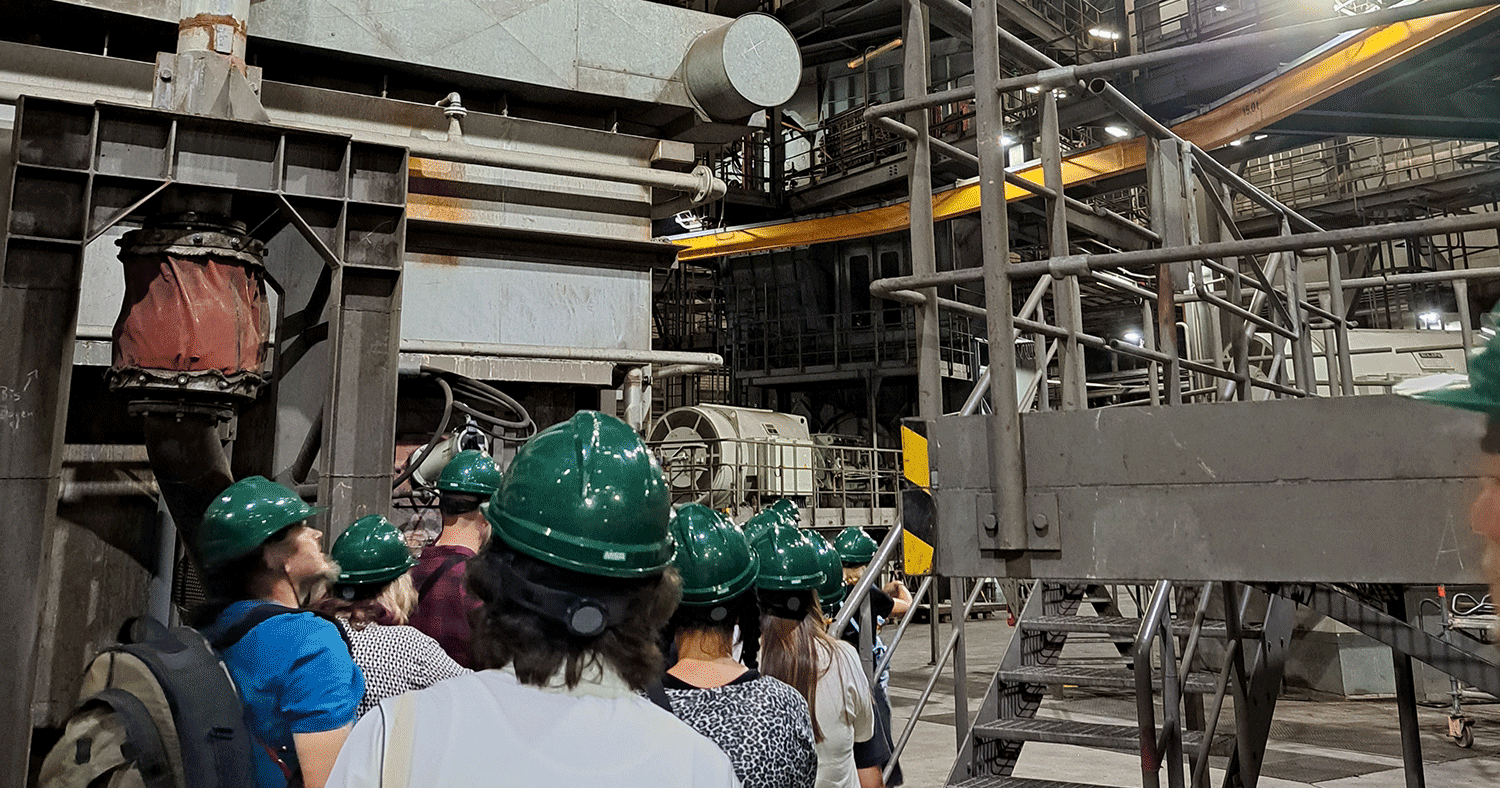 Schüler mit dunkelgrünen Kopfschutz laufen in eine Fabrik.